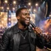 Kevin Hart performing stand-up comedy on an arena stage with a microphone in front of a large cheering crowd.